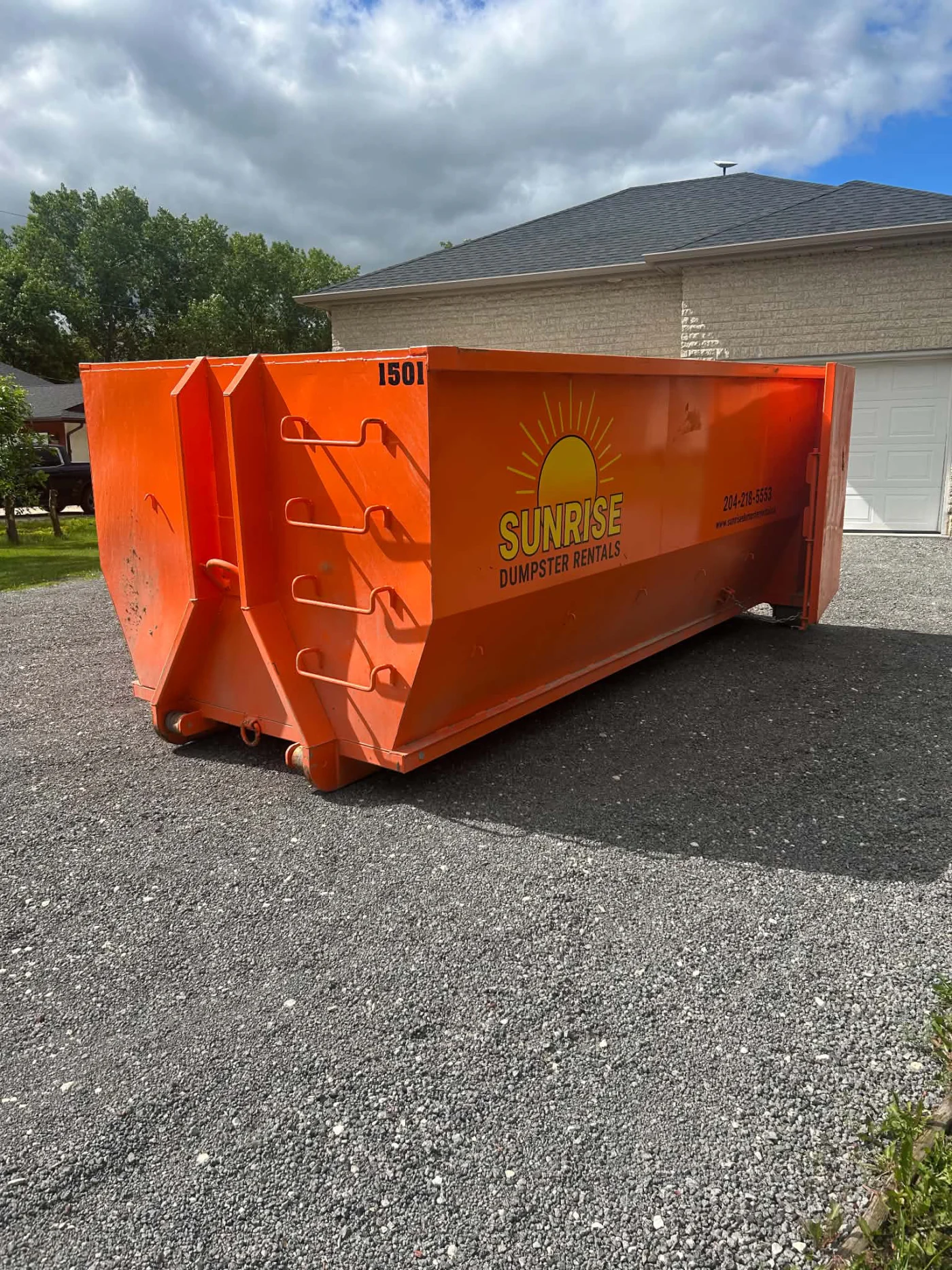 Sunrise Dumpster Rental orange roll-off bin delivered to a residential driveway